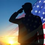Silhouette of saluting soldier in front of US flag and sunset